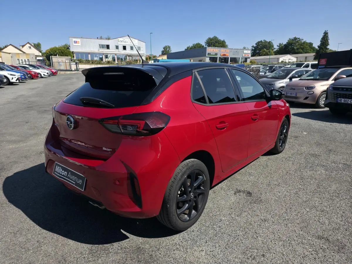 Opel Corsa rouge 3/4 arrière droit avec toit noir, jantes noires et vitres arrière surteintées.