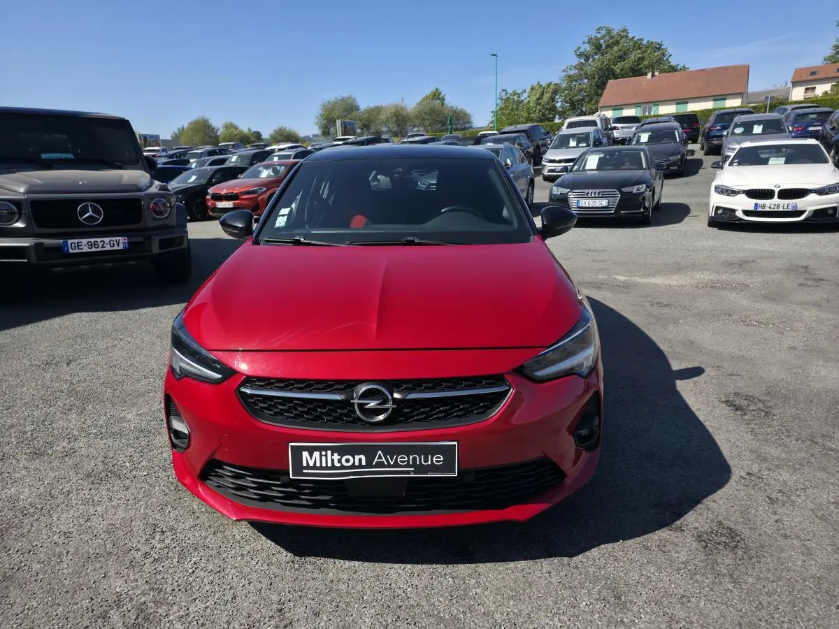 Vue avant d'une Opel Corsa rouge métallisée avec calandre noire et toit noir, stationnée en extérieur.