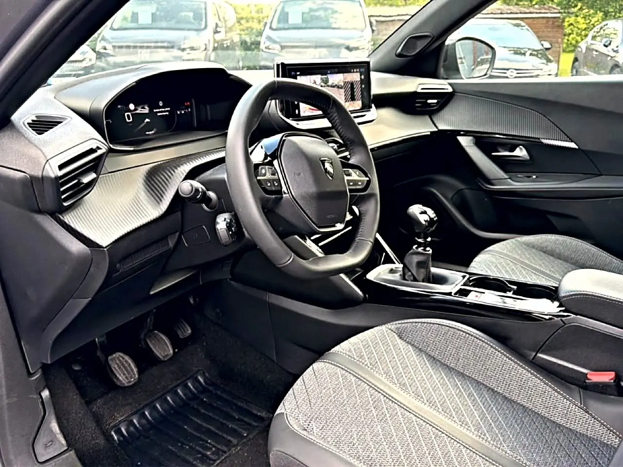 Intérieur de la Peugeot 2008 1.2 100 allure 2025 vu côté conducteur, volant compact, sellerie tissu gris et levier manuel.