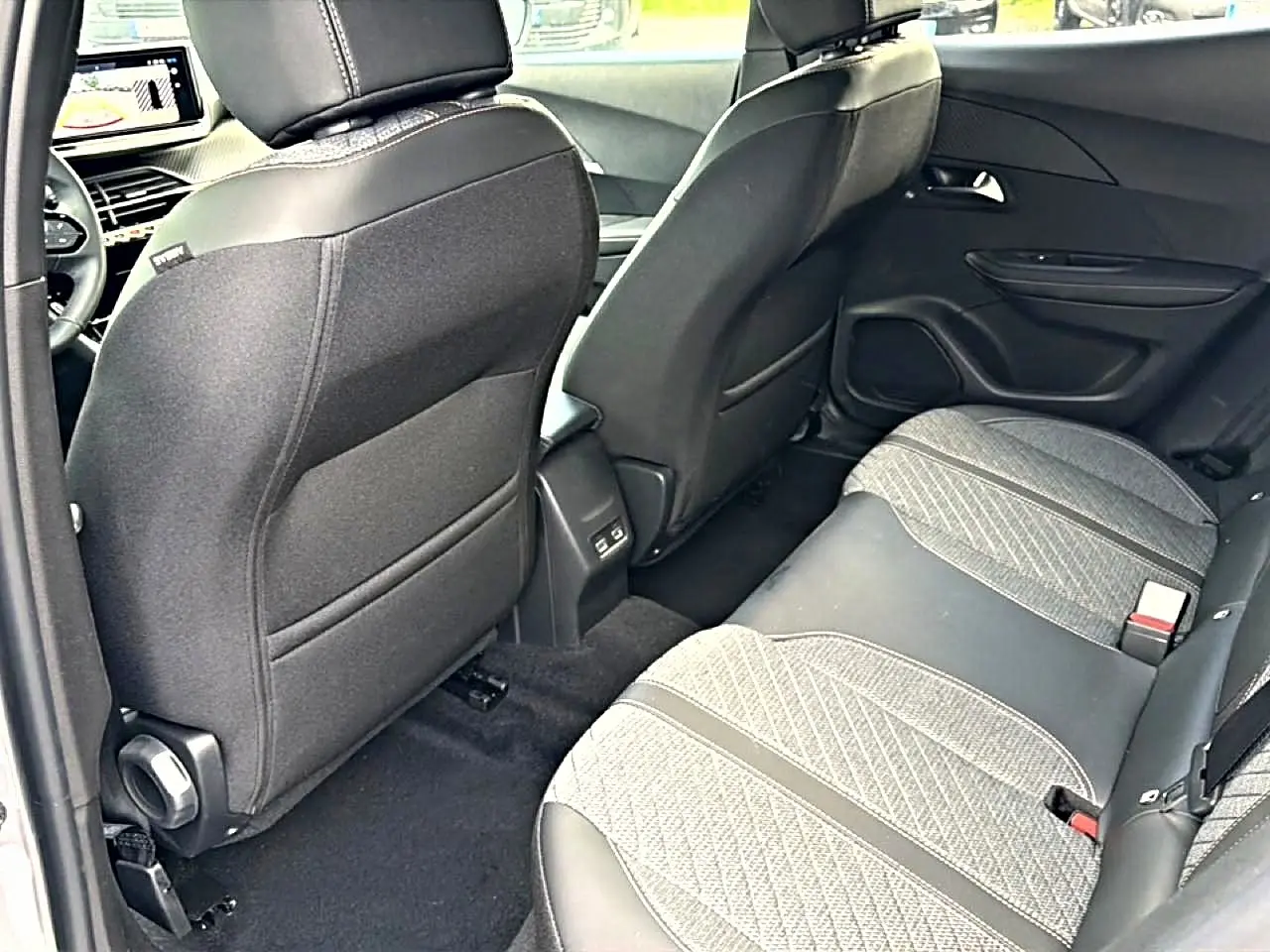 Vue intérieure arrière droite du Peugeot 2008 2025 gris artense, montrant les sièges arrière en tissu embossé et les dossiers avant noirs.