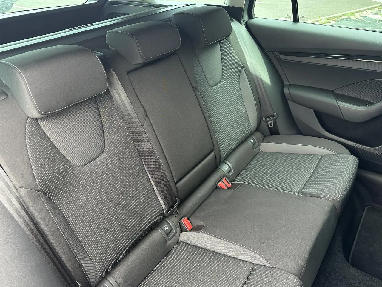 Vue latérale des sièges arrière noirs en tissu de la Skoda Octavia Combi 2024, avec appuie-têtes et ceintures visibles.