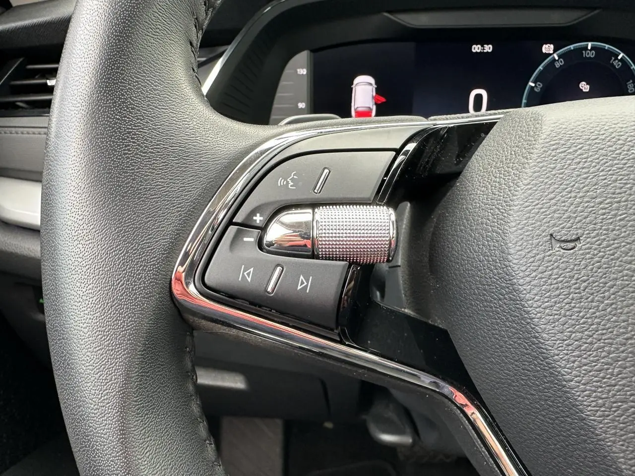 Gros plan sur les commandes gauche du volant cuir de la Skoda Octavia Combi gris graphite, tableau de bord numérique visible.