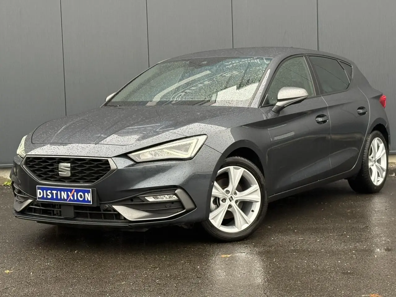 SEAT Leon 1.5 e-TSI 150 DSG7 FR gris magnétique vue 3/4 avant sous la pluie avec jantes alliage 17 pouces.