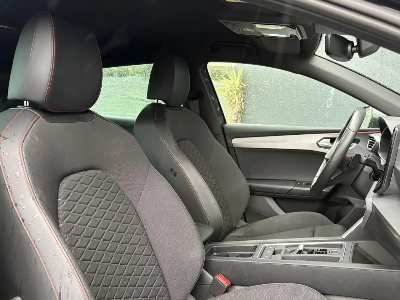 Vue intérieure côté droit du SEAT LEON 2024 FR avec sièges tissu noir à surpiqûres rouges et ciel de toit noir.