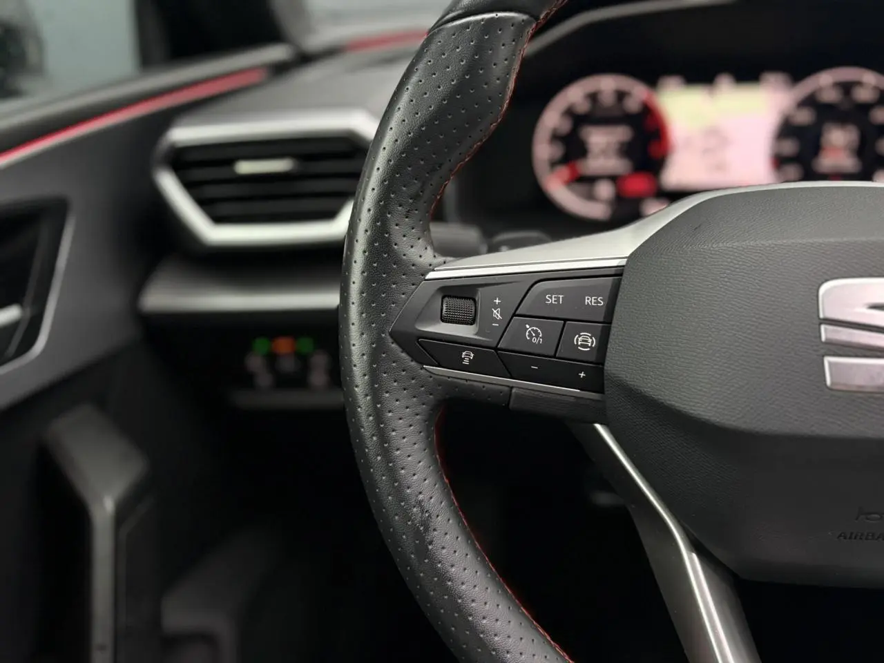 Gros plan sur le volant cuir perforé avec commandes multifonctions du SEAT Leon 2024, ambiance intérieure sombre.