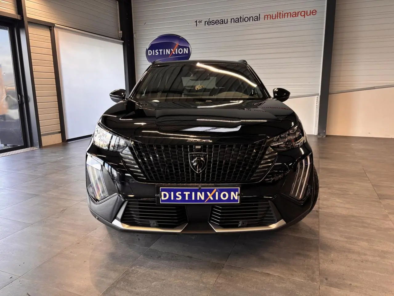 Vue frontale d'un Peugeot 2008 noir brillant avec calandre noire et feux LED distinctifs en showroom.