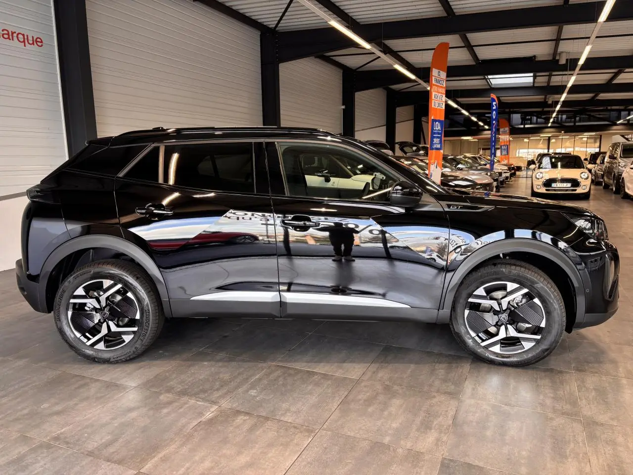 Profil côté gauche du Peugeot 2008 noir brillant avec jantes alliage bi-ton et toit Black Diamond en showroom.