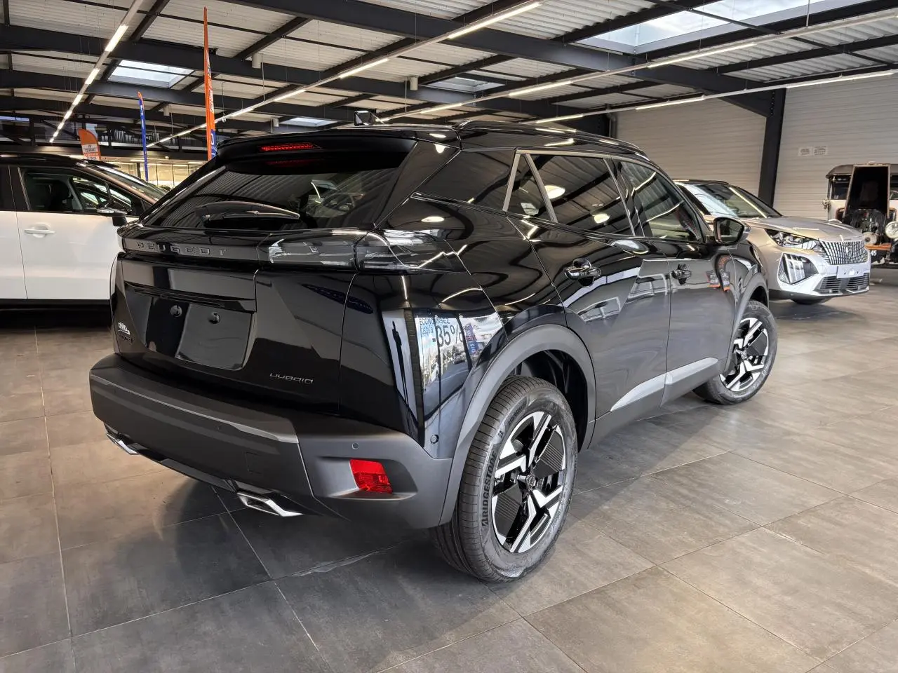 Peugeot 2008 hybride noire vue 3/4 arrière droit en showroom avec jantes bi-ton et feux LED griffés.