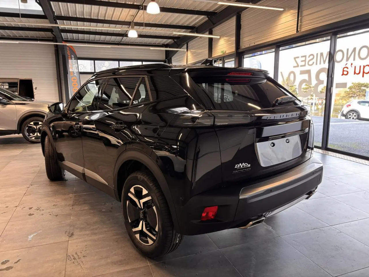 Vue 3/4 arrière droite d'un Peugeot 2008 noir brillant en showroom avec feux arrière LED et jantes bi-ton.