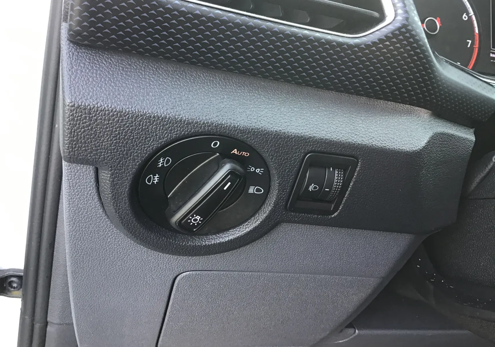 Détail du tableau de bord côté gauche du Volkswagen T-Cross blanc 2021, avec commande des phares et réglage du faisceau lumineux.