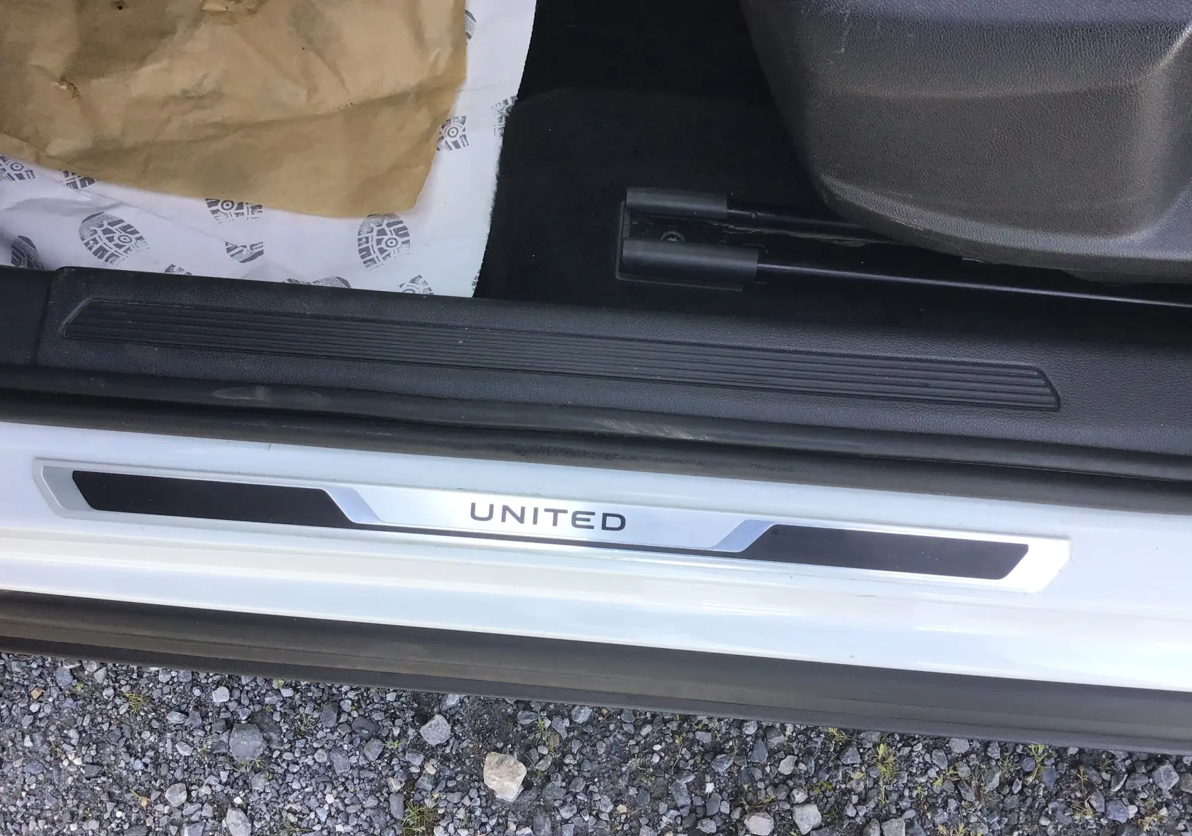 Gros plan sur la plaque de seuil de porte "UNITED" du Volkswagen T-Cross blanc, côté gauche, avec intérieur noir visible.