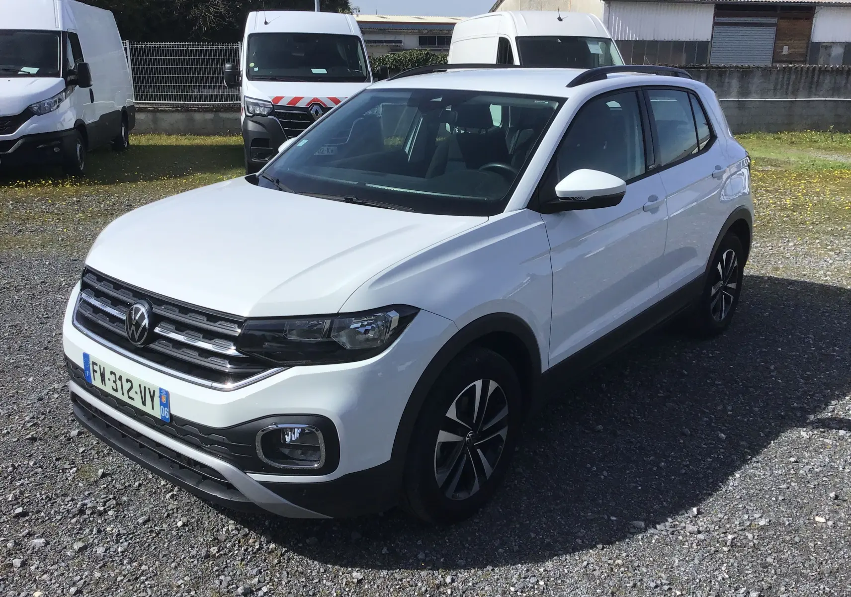 Volkswagen T-Cross blanc en 3/4 avant droit, avec jantes alliage et barres de toit noires visibles.