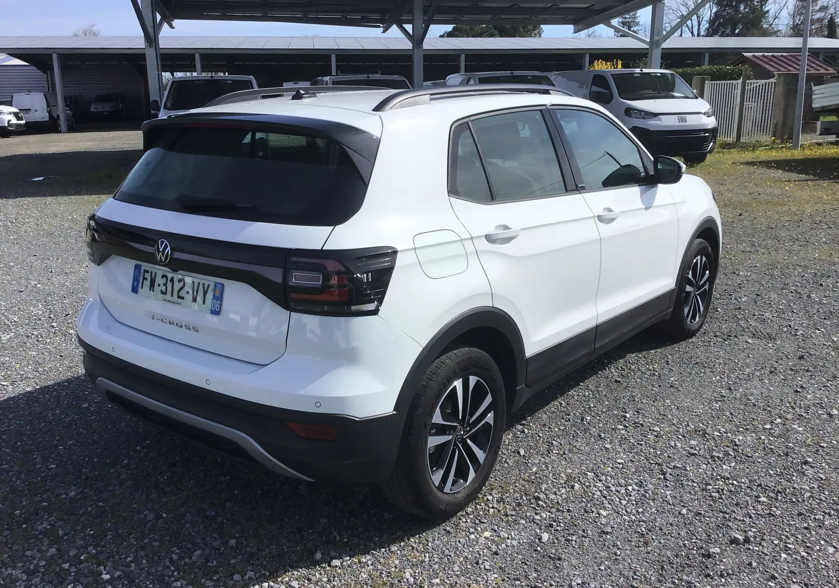 Vue 3/4 arrière droite d'un Volkswagen T-Cross blanc 2021 avec jantes alliage noires et feux arrière foncés.