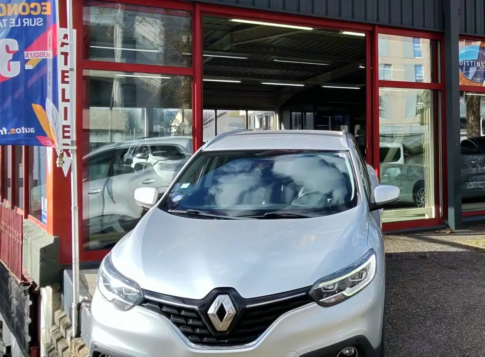 Renault Kadjar gris platine vu de face, stationné devant un garage avec enseigne AD Expert.