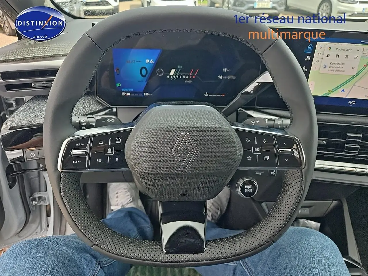 Vue intérieure centrée sur le volant noir perforé de la Renault Clio VI avec tableau de bord numérique et écran tactile.