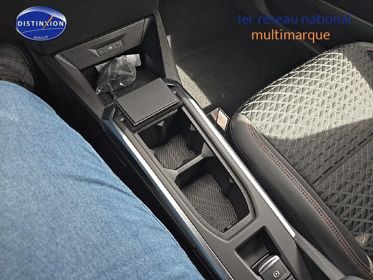 Vue rapprochée de l'accoudoir central avec rangement et console de la Renault Clio VI gris rafale, sièges tissu noir.
