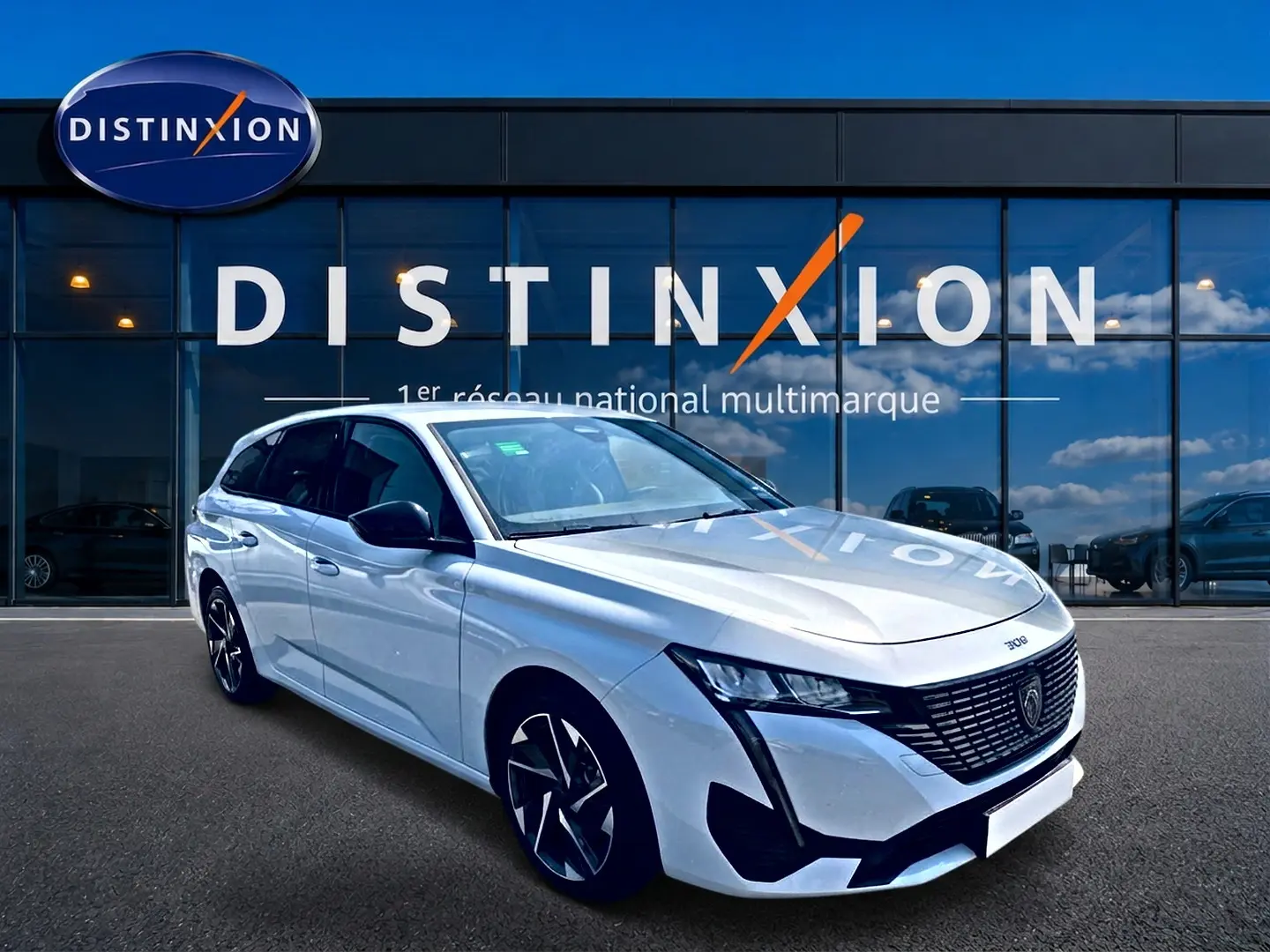 Peugeot 308 SW blanche vue en 3/4 avant droit, avec jantes alu et calandre noire distinctive devant un showroom Distinxion.