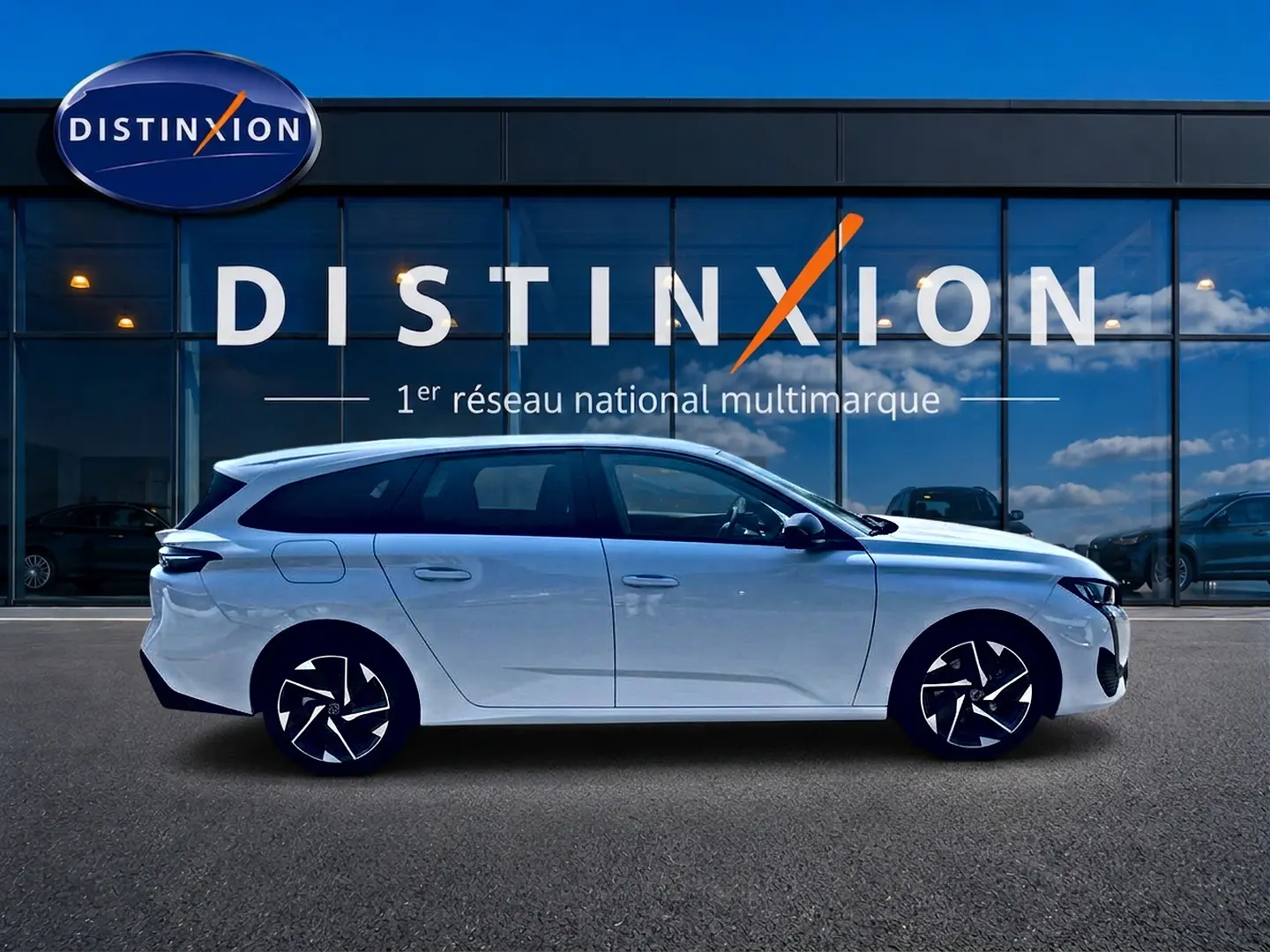 Profil droit d'un Peugeot 308 SW blanc 2025 avec jantes alu noires et vitres arrière surteintées, devant une vitrine Distinxion.