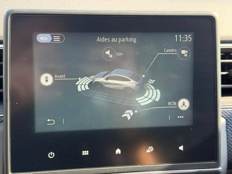 Écran tactile montrant l'aide au parking du Renault Arkana gris métallisé en vue 3/4 arrière avec capteurs activés.