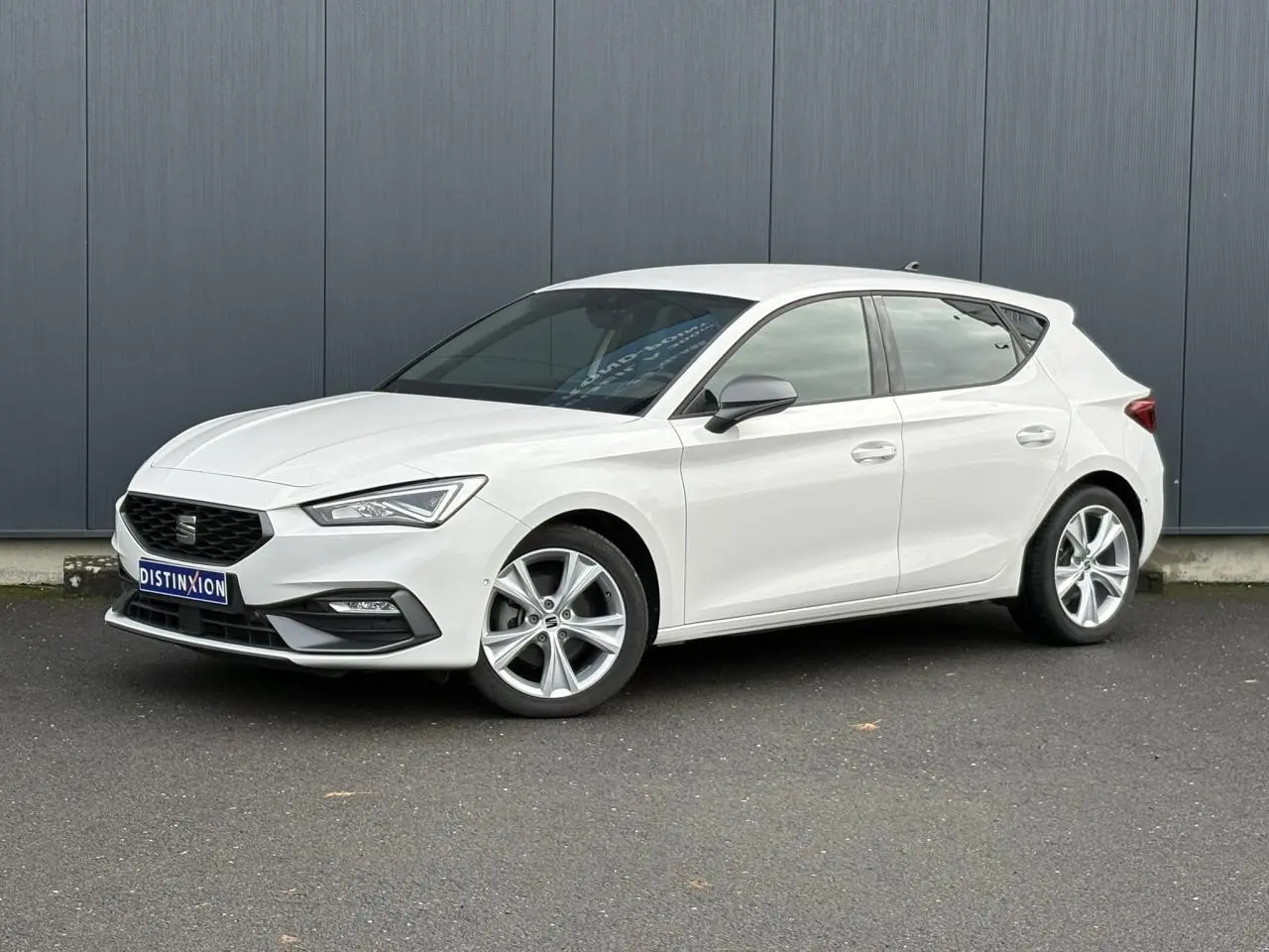 Vue 3/4 avant droite d'une SEAT Leon 1.5 e-TSI 150 DSG7 FR blanche avec jantes alliage 17 pouces et vitres surteintées.