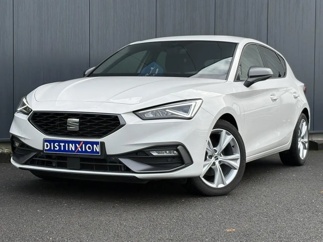 Vue 3/4 avant droite d'une SEAT Leon blanche 2024 avec jantes alliage et calandre noire distinctive.