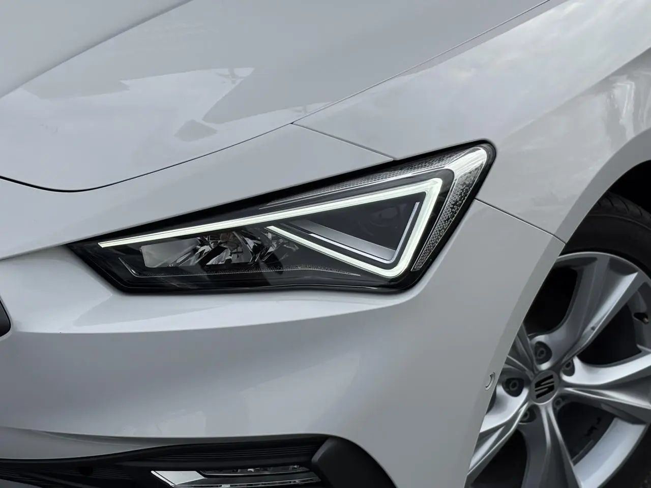 Gros plan sur le phare avant droit et la jante alliage 17 pouces d'une SEAT Leon blanche 2024 finition FR.