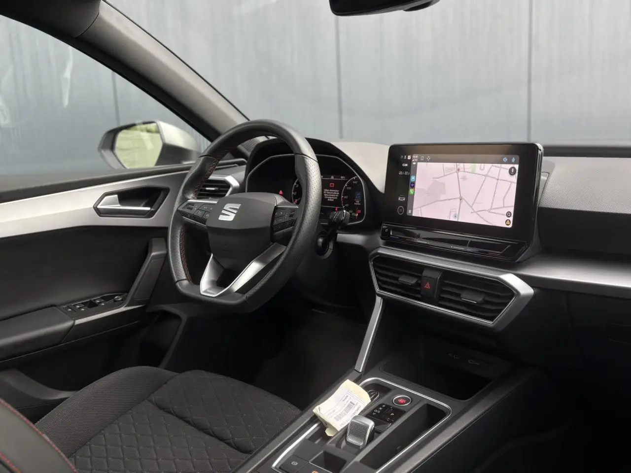 Intérieur côté conducteur du SEAT Leon blanc 2024, volant cuir multifonction et écran tactile de navigation visible