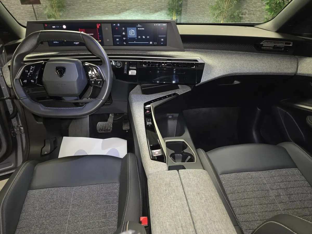 Vue intérieure avant du Peugeot 3008 gris 2025, mettant en valeur le tableau de bord numérique et la console centrale avec décor tissu Rimini.