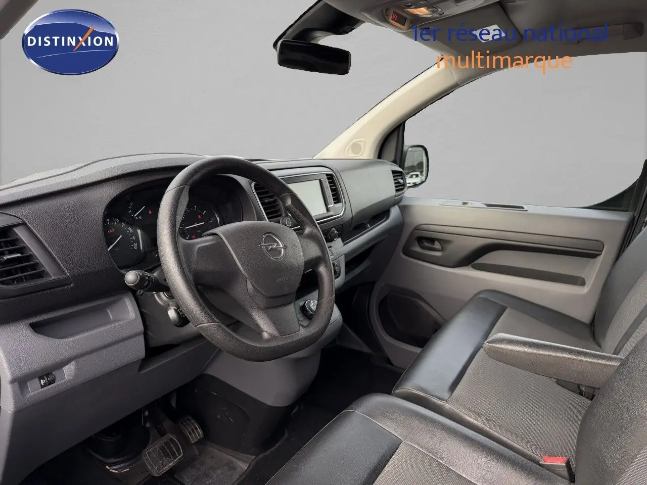 Vue intérieure côté conducteur de l'Opel Vivaro 2020, tableau de bord et sièges en tissu noir visibles.