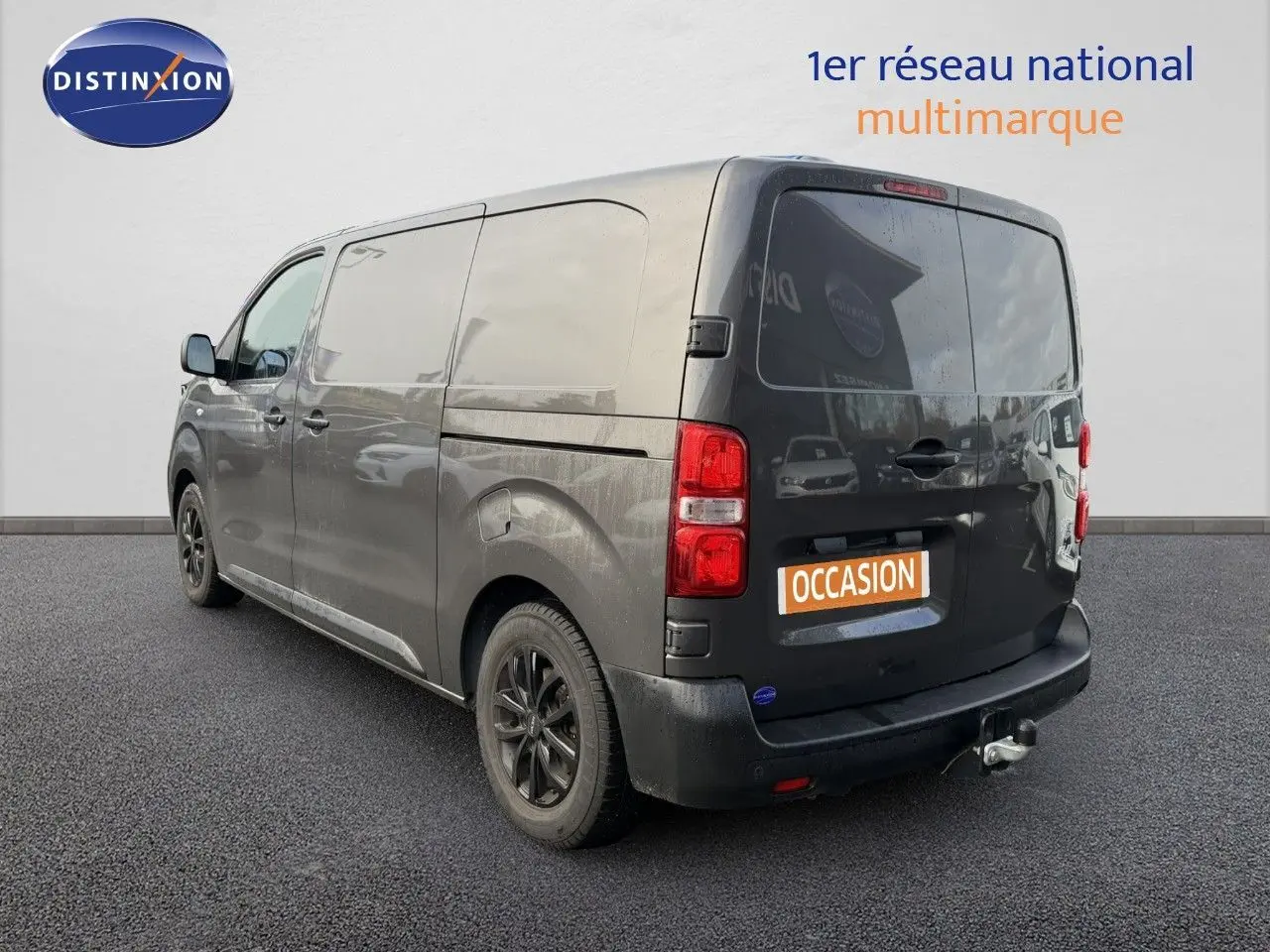 Vue 3/4 arrière droite d’un Opel Vivaro gris titane métal avec attelage et jantes noires, sur fond neutre.