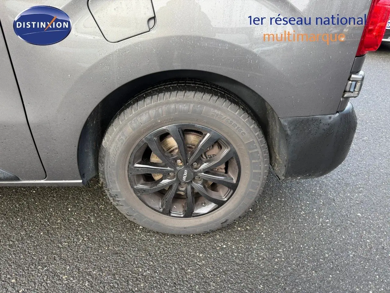 Gros plan sur la roue arrière droite d’un Opel Vivaro gris titane métal avec jante noire et carrosserie mouillée.