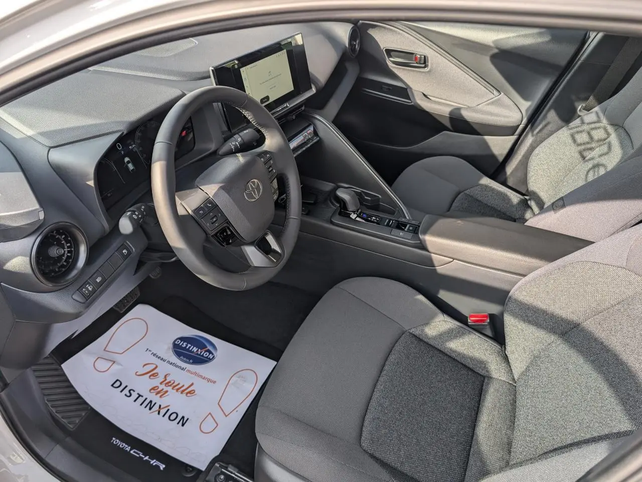 Vue intérieure côté conducteur du Toyota C-HR 2024, sellerie tissu gris foncé et tableau de bord avec écran tactile.