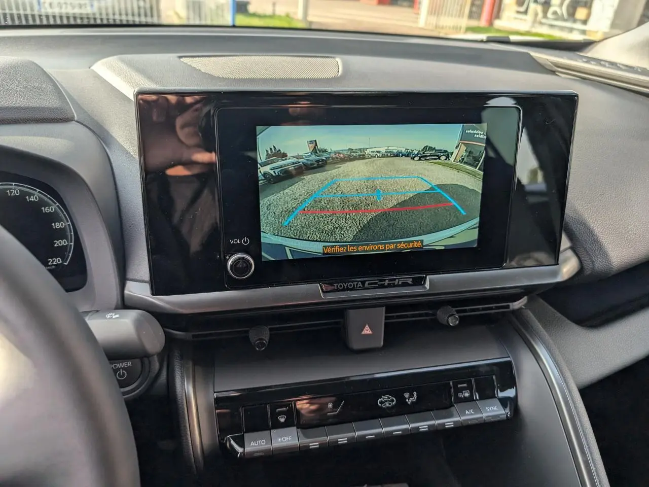 Vue intérieure centrée sur l'écran tactile affichant la caméra de recul du Toyota C-HR blanc, tableau de bord visible.