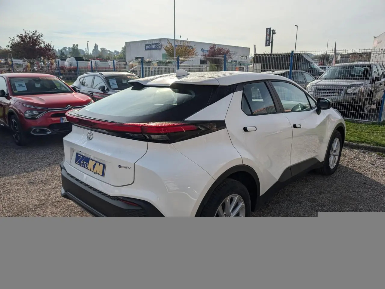 Toyota C-HR blanc vu en 3/4 arrière droit, avec feux arrière full LED et poignées affleurantes noires.
