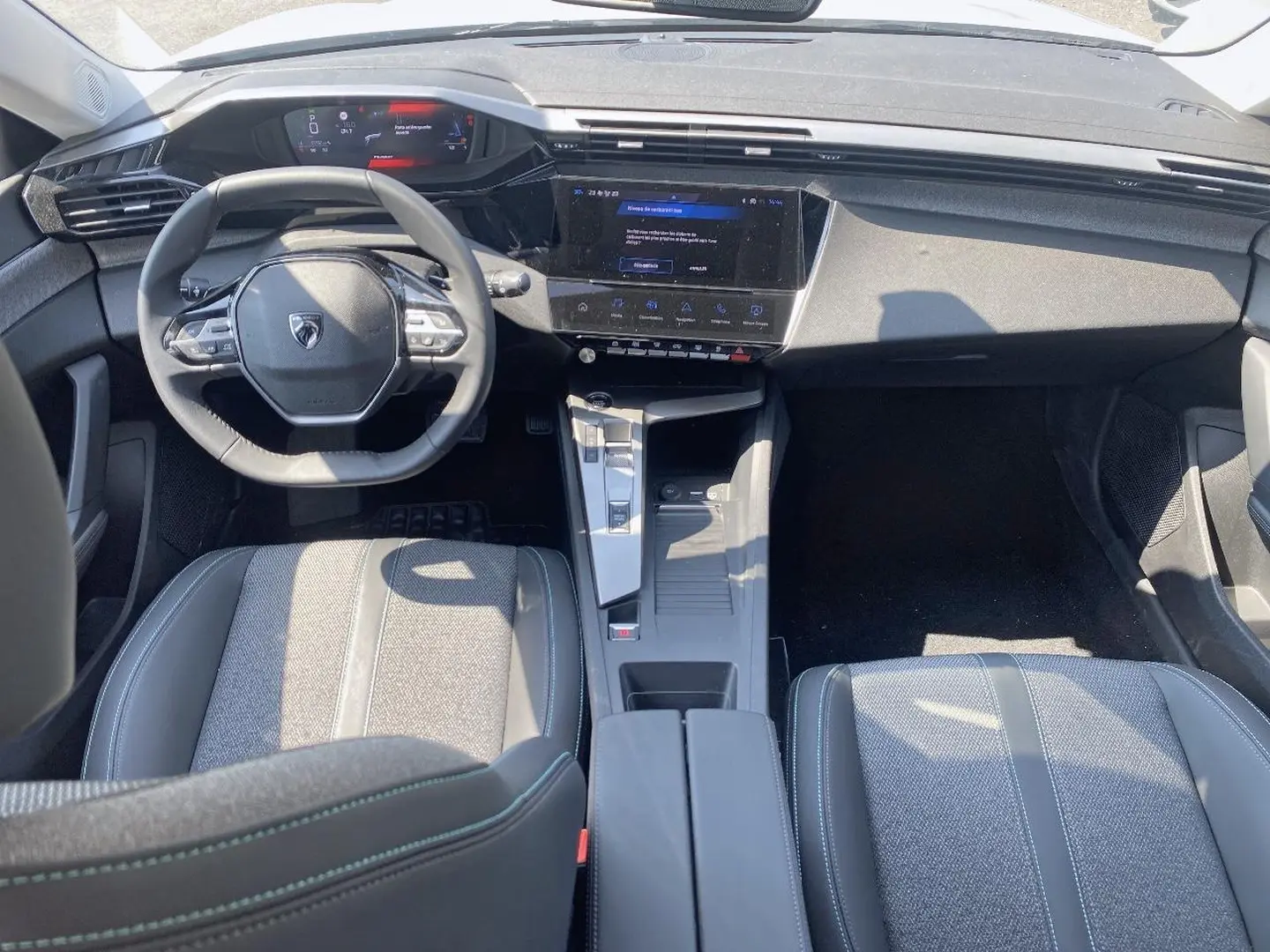 Vue intérieure avant de la Peugeot 308 SW 2025, tableau de bord noir avec écran tactile et volant multifonction.