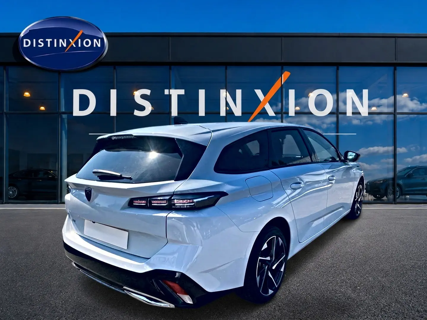 Vue 3/4 arrière droite d'une Peugeot 308 SW blanche 2025 avec jantes alu et vitres arrière surteintées, devant un showroom Distinxion.