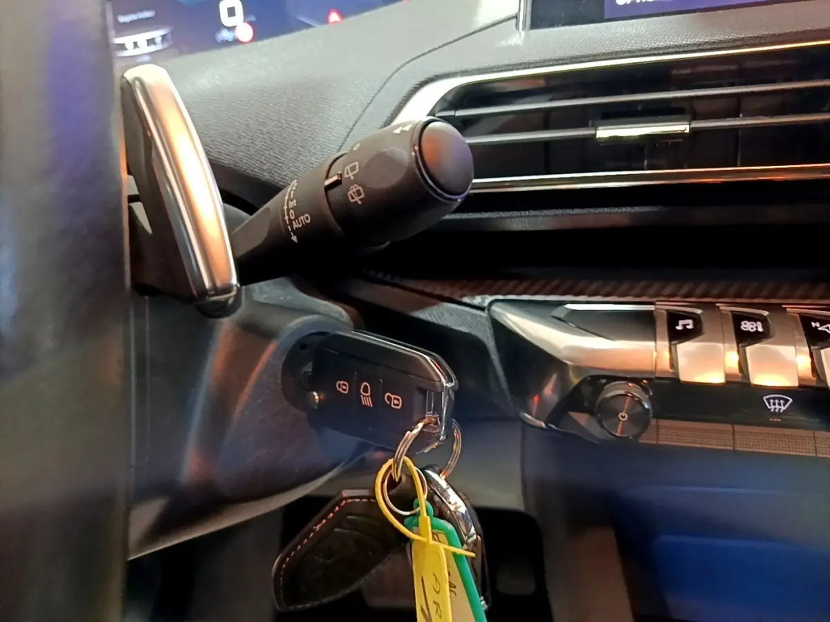 Gros plan intérieur sur la colonne de direction et le tableau de bord noir du Peugeot 5008 avec clé insérée et commandes tactiles visibles.