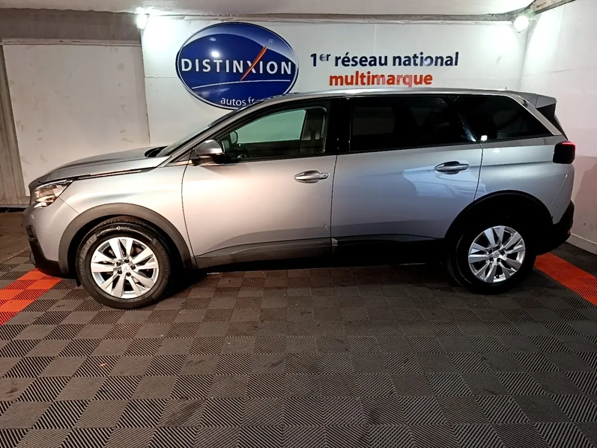 Vue de profil côté gauche d'un Peugeot 5008 gris clair 2020 stationné en intérieur avec logo Distinxion en arrière-plan.