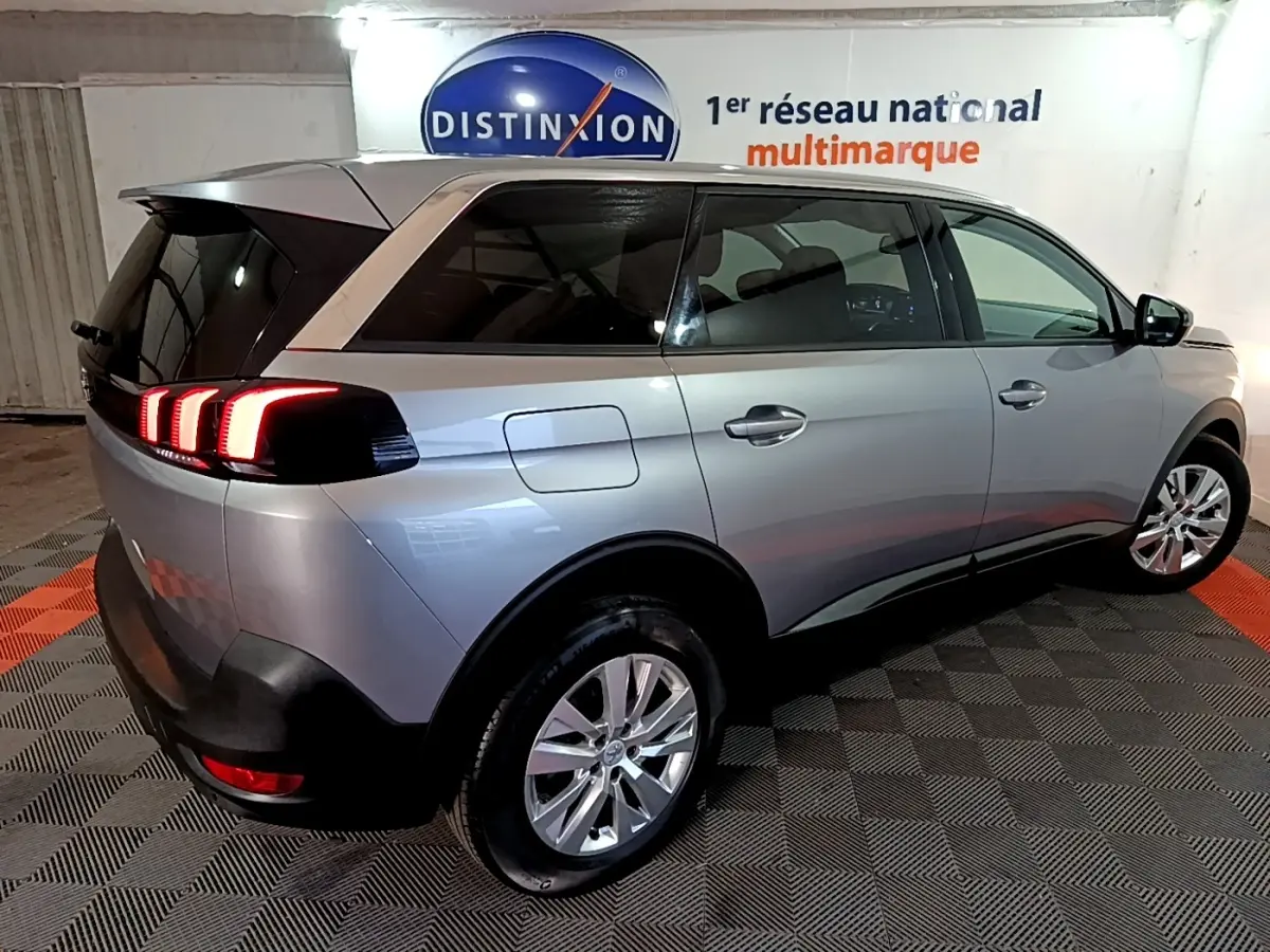 Peugeot 5008 gris clair vue 3/4 arrière droit, feux arrière LED allumés, intérieur visible à travers les vitres teintées.