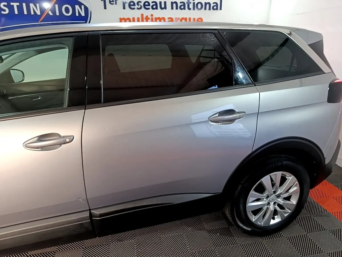 Vue latérale côté droit d’un Peugeot 5008 gris clair, mettant en valeur les portes arrière et la roue arrière dans un intérieur showroom.
