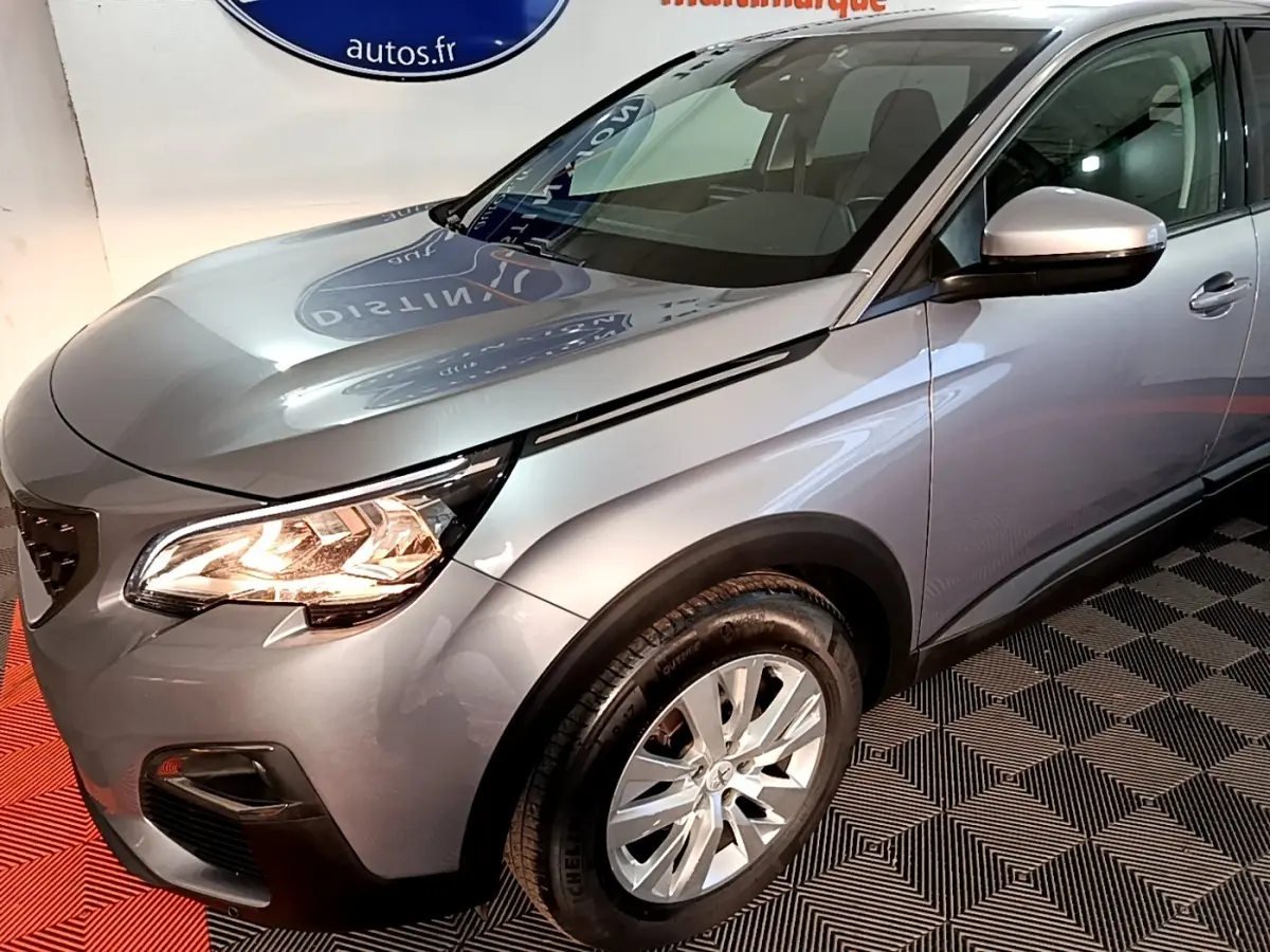 Vue 3/4 avant droit d’un Peugeot 5008 gris clair avec phares allumés et jantes alliage visibles.