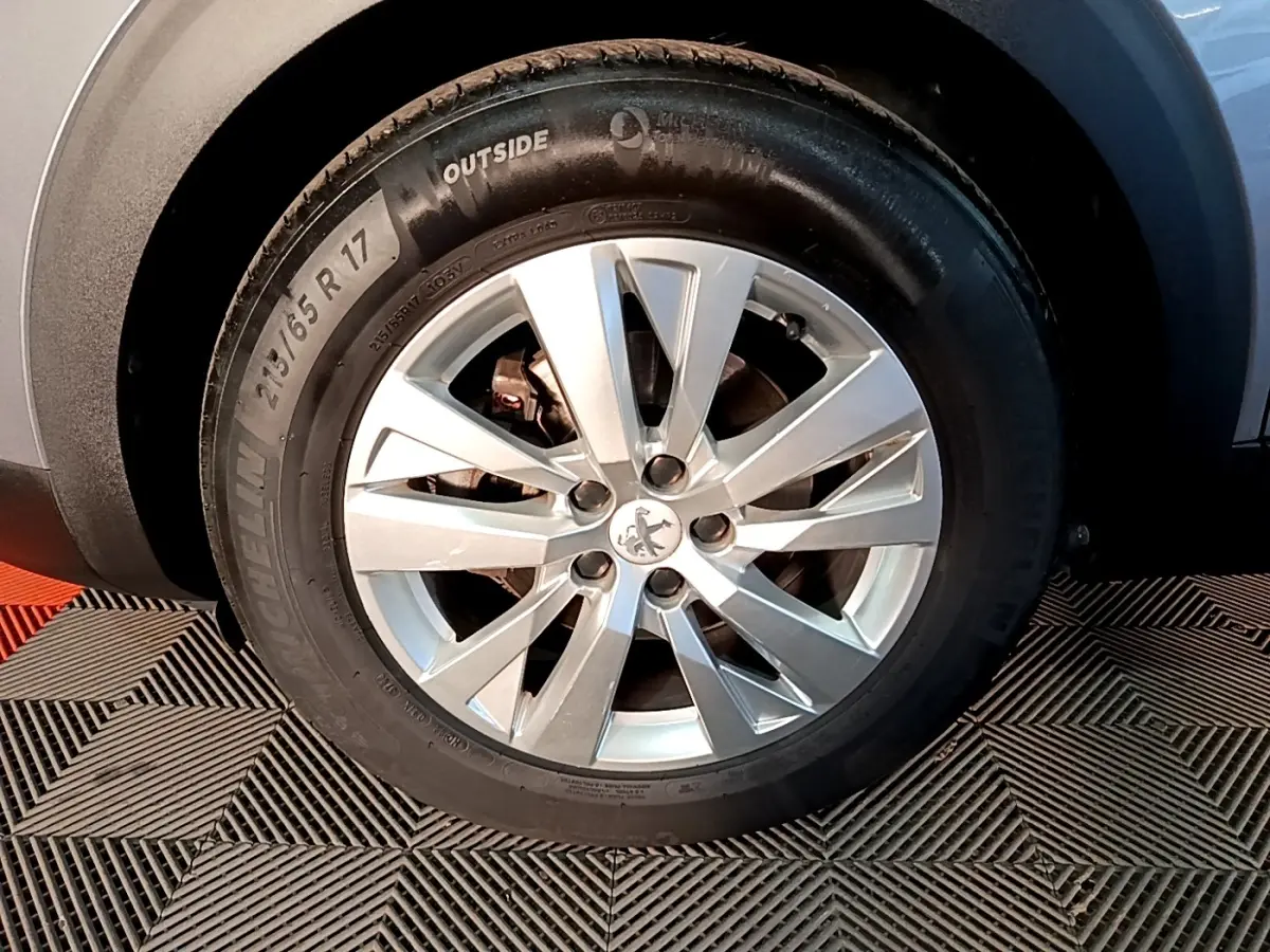 Gros plan sur la roue avant droite d’un Peugeot 5008 gris clair, avec jante alliage à cinq doubles branches.