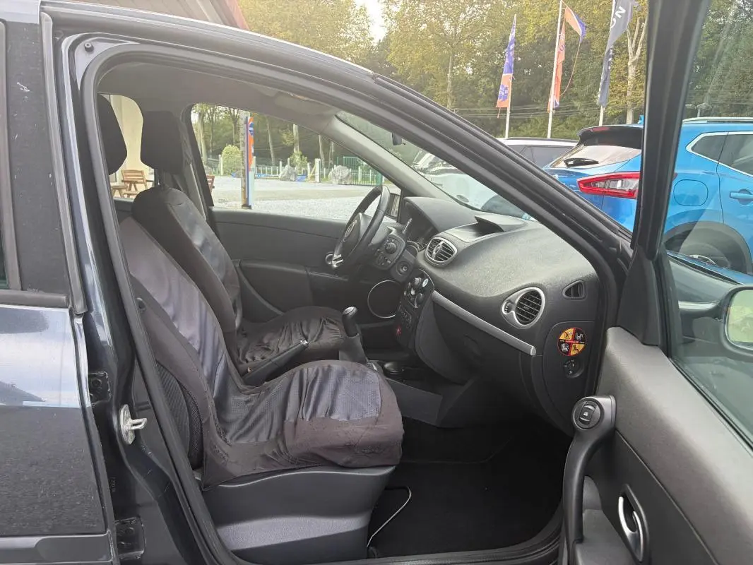 Vue intérieure côté conducteur d'une Renault Clio III gris 2005, montrant les sièges et la console centrale avec boîte manuelle.