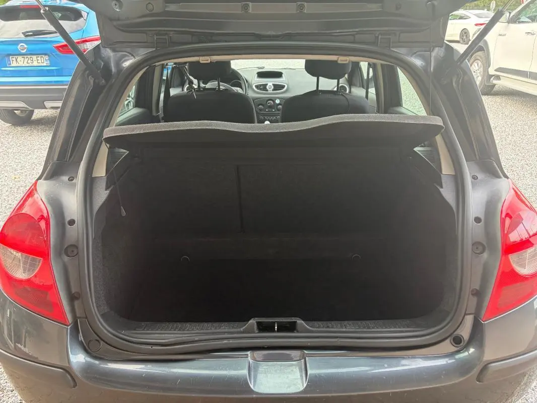 Coffre ouvert d’une Renault Clio III gris 2005, vue arrière montrant l’espace de chargement et l’intérieur des sièges avant.