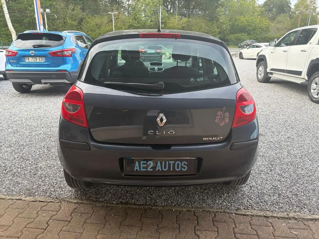 Vue arrière d'une Renault Clio III gris foncé de 2005 avec un autocollant fleur rouge sur le coffre.