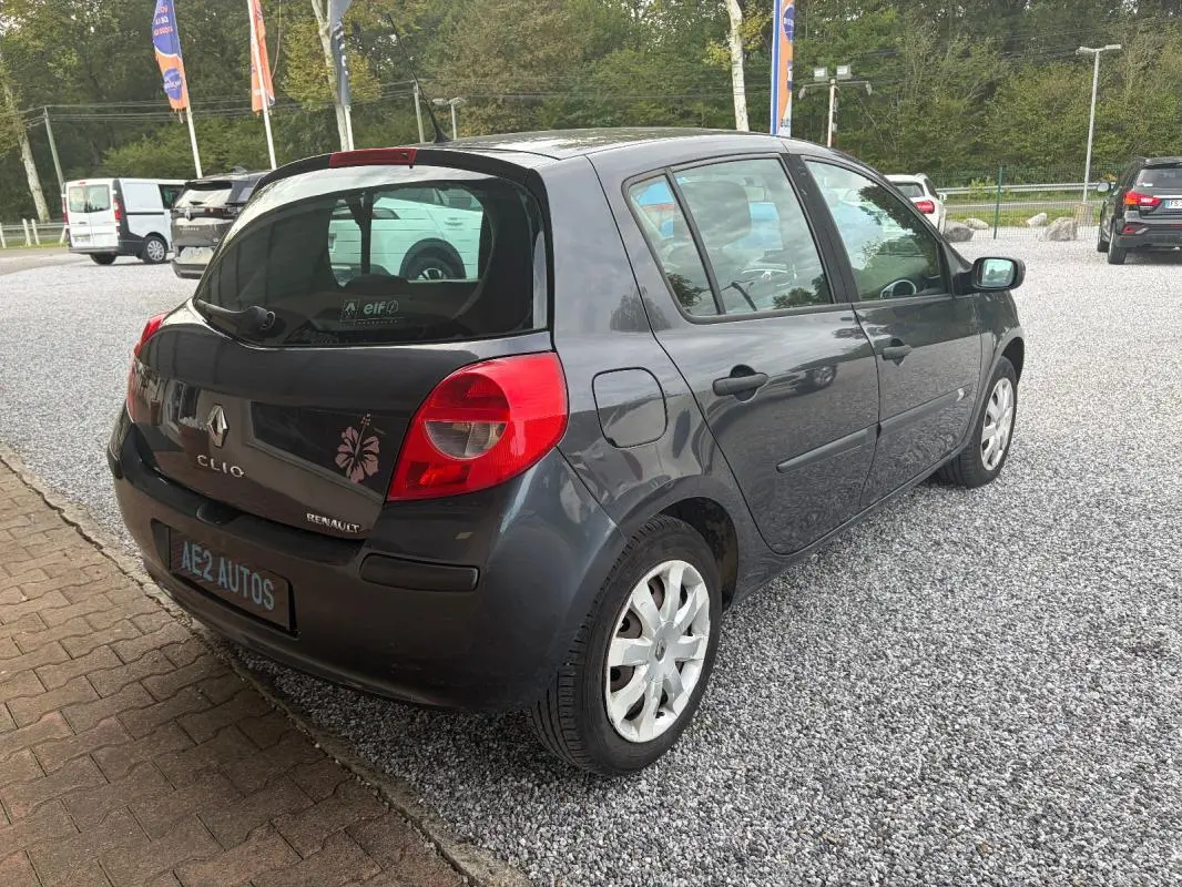 Vue 3/4 arrière droite d'une Renault Clio III gris foncé de 2005 avec jantes acier et feux arrière rouges.