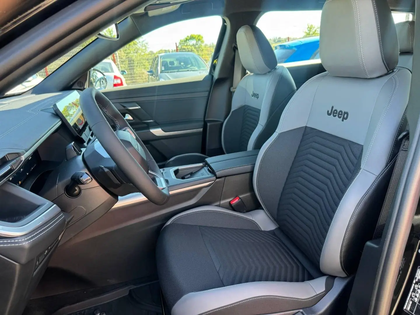 Intérieur avant droit du Jeep Compass 2026 avec sièges tissu gris/anthracite et logo Jeep brodé sur appuie-têtes.