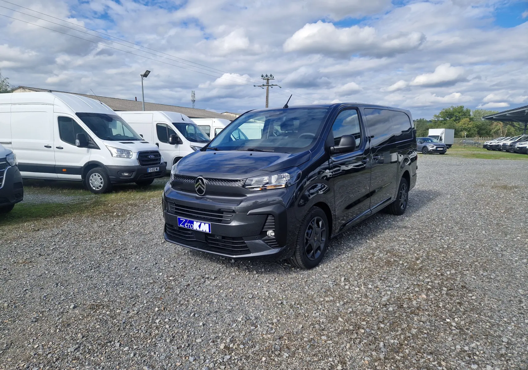 Vue 3/4 avant d'un Citroën Jumpy XL gris titane avec jantes tôles 17 pouces sur un parking extérieur.