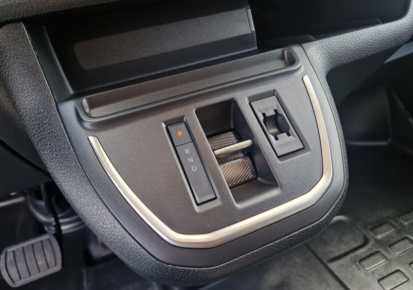 Gros plan sur la commande de boîte automatique et prise 12V du Citroën Jumpy XL gris titane, intérieur noir.