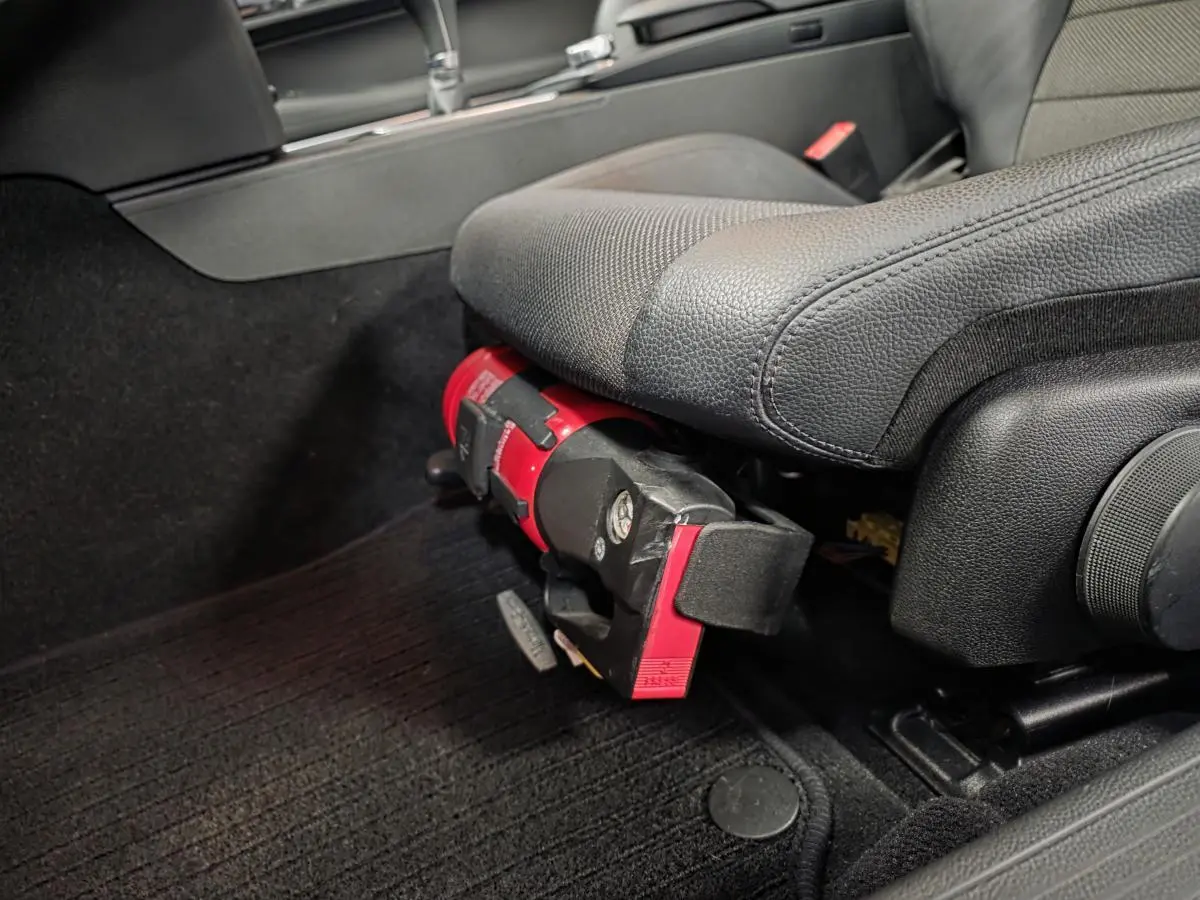 Vue rapprochée sous le siège conducteur d'une Mercedes Classe E Coupé gris, montrant un extincteur rouge fixé au cadre.